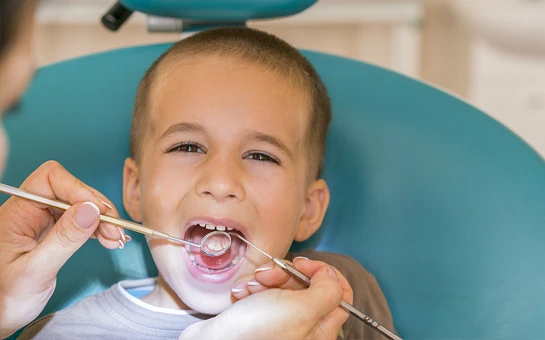 A young boy sitting in an exam chair with mouth open while a dentist examines his teeth